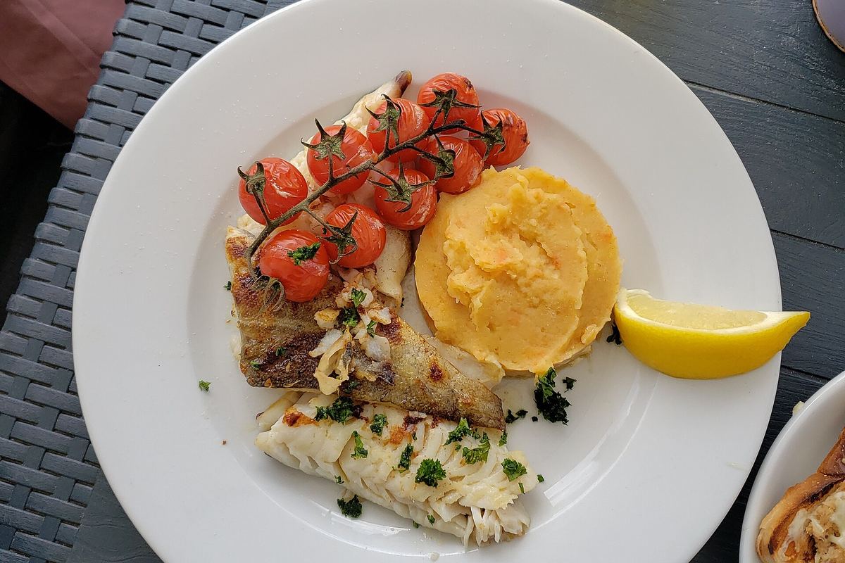 Cod fillet with roasted cherry tomatoes and a lemon wedge on a white plate