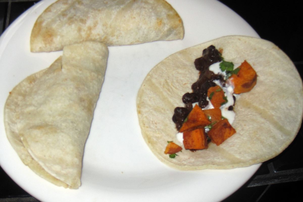 Two soft tortillas with black beans and roasted vegetables on a white plate