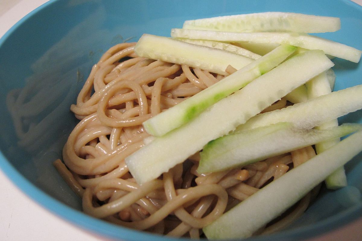 Bowl of noodles in peanut sauce topped with cucumber sticks